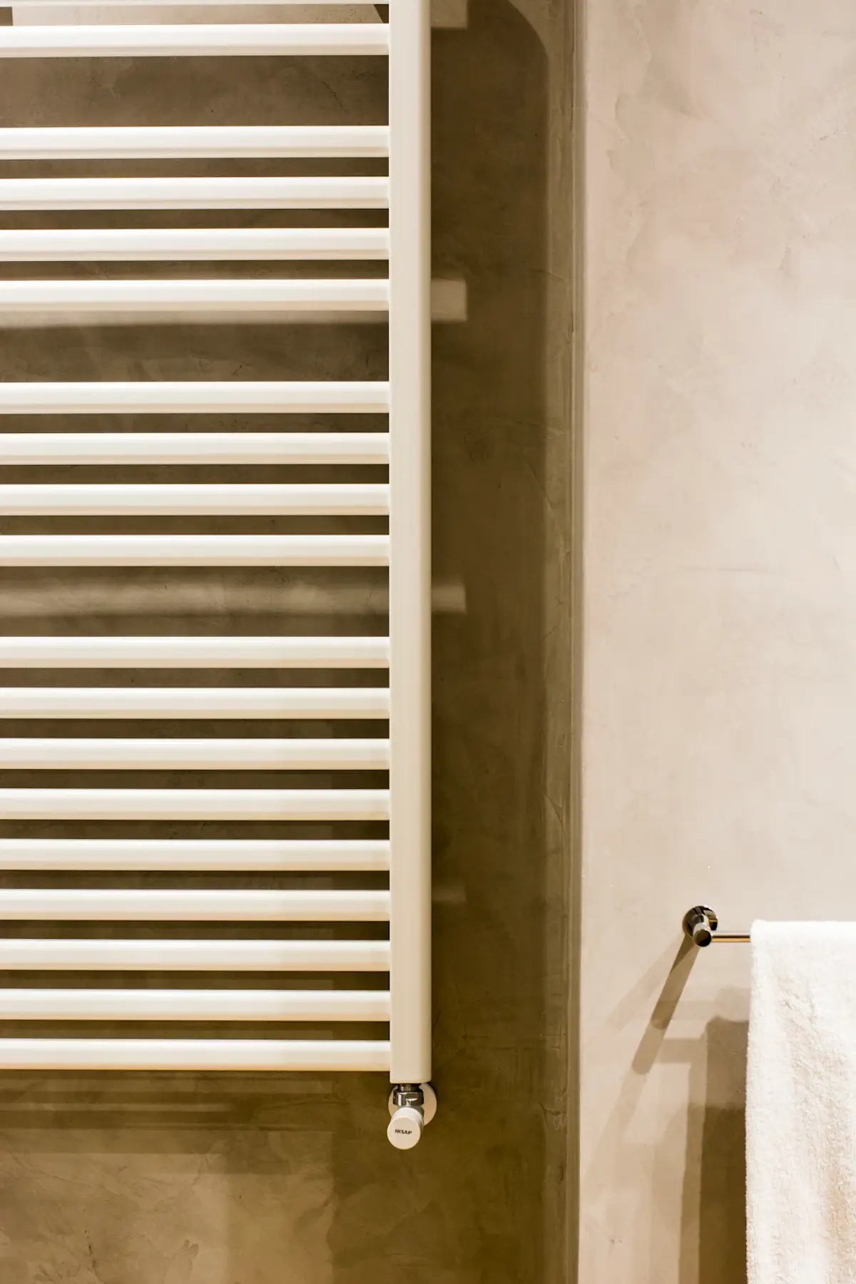 white wall mounted towel radiator with horizontal bars and a towel hanging on a chrome hook in a modern bathroom